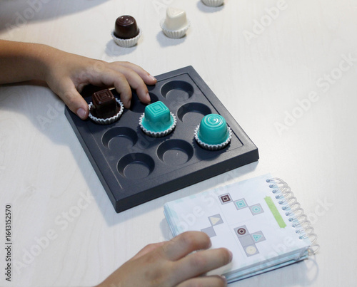 Board game, a visual perception exercise for visual therapy. Pieces of different colors and shapes are placed on the board according to rules. Children's hands playing a board game with pieces.