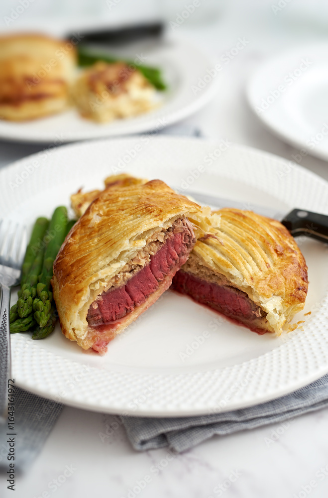 Individual beef wellington and vegetables on white plate. Individual beef wellington and vegetables on white plate.