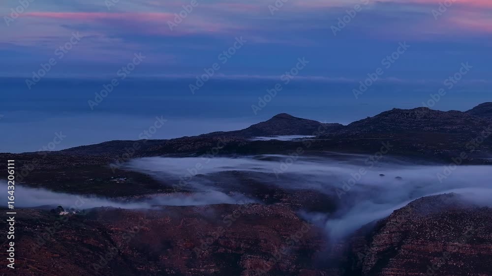 Aerial view of low-lying fog clinging to the slopes of rugged mountains under a dusky, twilight sky, creating a dramatic landscape, Cape Town, Western Cape, South Africa. Aerial view of low-lying fog clinging to the slopes of rugged mountains under a dusky, twilight sky, creating a dramatic landscape, Cape Town, Western Cape, South Africa.
