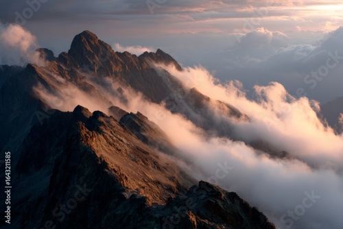 Dramatic mountain range at sunrise with low clouds, mist, and warm light across jagged peaks.