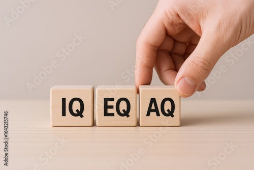 Hand Arranging Wooden Blocks Displaying IQ, EQ, and AQ for Intelligence, Emotional, and Adaptability Quotient