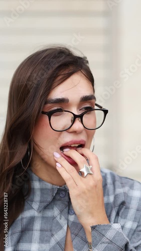 Brunette woman in glasses puts clear aligners on her teeth and smiles at the camera in a bright, friendly setting