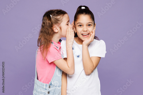 Little two friends kids children girls 9-10 year old wearing casual clothes together whisper gossip and tells secret behind her hand sharing news isolated on plain purple background Lifestyle concept