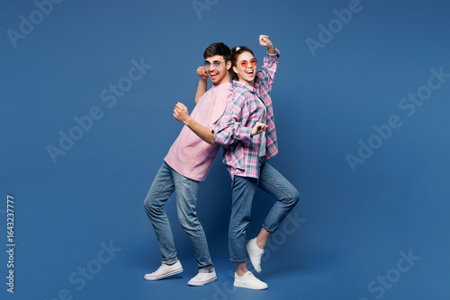 Full body young happy couple two friends family man woman wear pink casual clothes sunglasses together doing winner gesture celebrate clench fist stand back to back isolated on plain blue background.