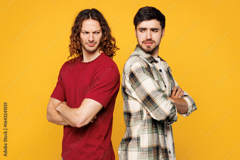 Obraz premium Young offended two friends buddies men wears casual clothes together hold hands crossed folded stand back to back isolated on plain yellow orange color background studio portrait. Lifestyle concept.