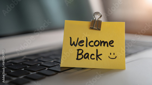Welcome back message on yellow sticky note with clip placed on laptop keyboard surface