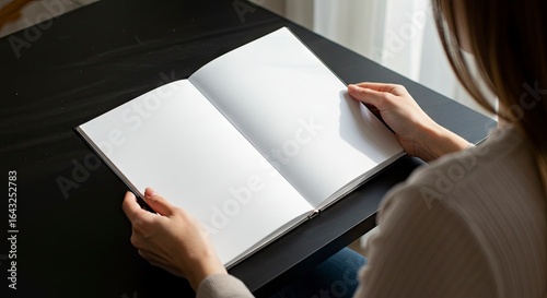Woman holding open blank book on black table seen from over shoulder
