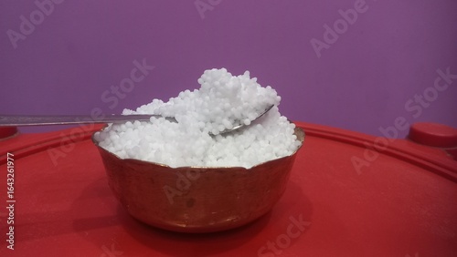 Photos This image shows a metal bowl filled with white sago pearls (sabudana) placed inside a larger brass plate