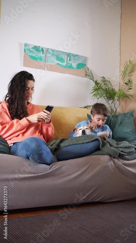 Mother using smartphone while son eats with dog on sofa