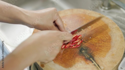 A video shows a bright red chili pepper being sliced on a clean wooden cutting board. chef carefully slices it beautifully shaped pieces, ready to add a vibrant colour and heat to the delicious dish. 