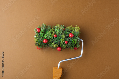 Bild auf Leinwand Festive paint roller with fir sprigs and red berries on warm brown backdrop promises cozy holiday makeover and playful Christmas mood