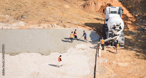 Aerial view of construction workers spreading and leveling fresh concrete from cement mixer truck at building site
