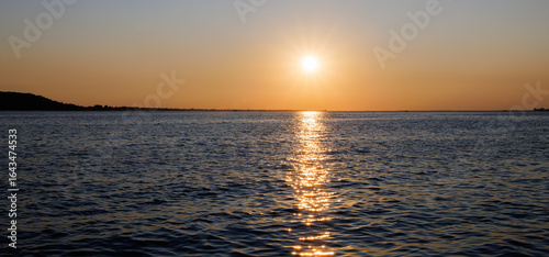 Golden sunset over the calm sea with gentle waves and a warm orange sky, reflecting sunlight across the water and creating a serene, peaceful coastal evening scene.
