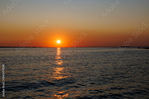 Vibrant sunset over calm ocean waters, casting a golden reflection across the waves under a warm orange and red sky, creating a peaceful and serene coastal evening scene.