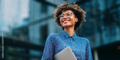 Smiling young black woman holding laptop outdoors