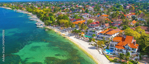 Fototapeta Naklejka Na Ścianę i Meble -  Coastal town aerial: turquoise waters, white sand beach, colorful houses, and boats