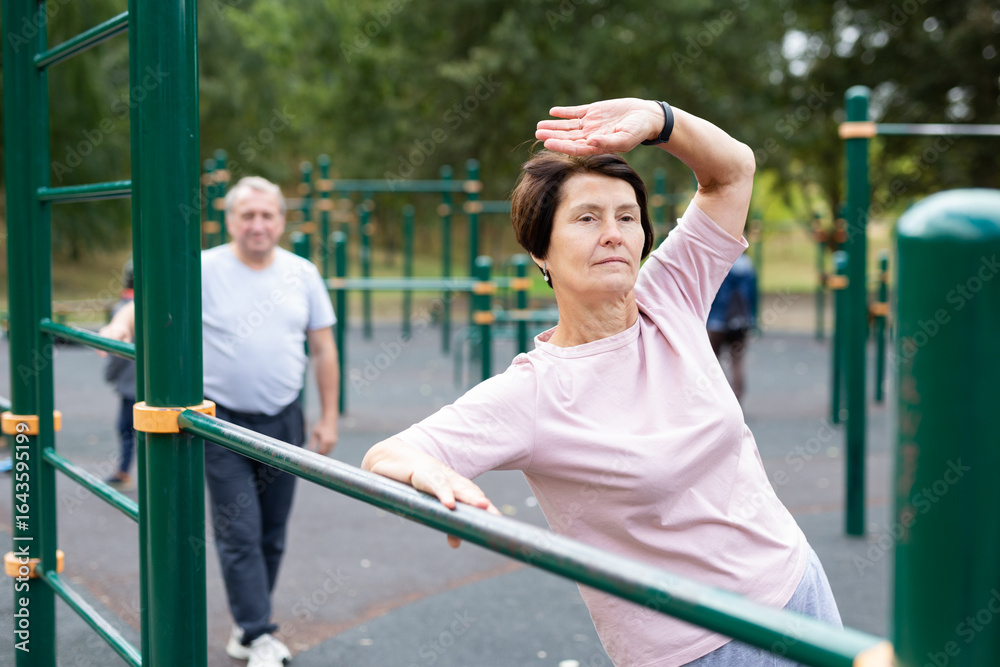 Fototapeta premium elderly woman doing exercises on a horizontal bar at an outdoor sports ground