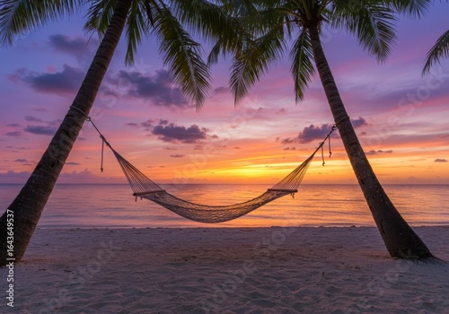 Fototapeta Naklejka Na Ścianę i Meble -  Tranquil beach hammock between palm trees at a vibrant tropical sunset
