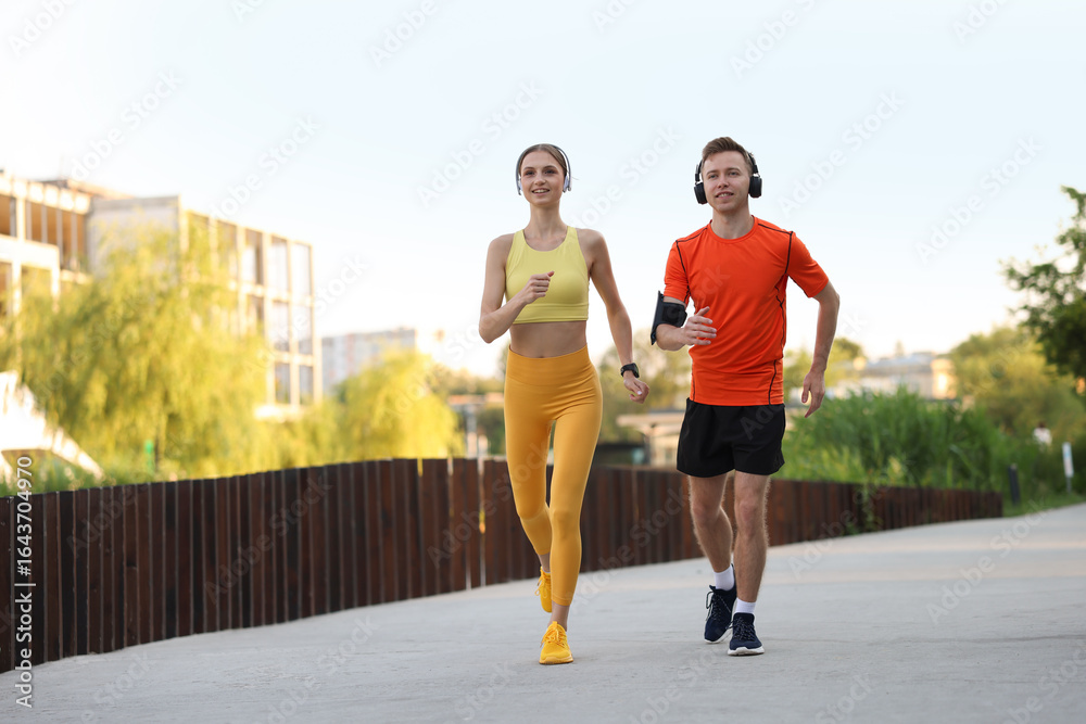 Obraz premium Happy couple in headphones running outdoors, low angle view. Morning exercise