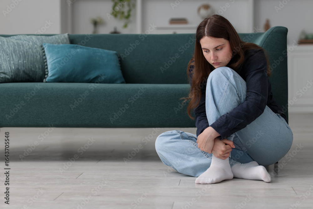 Obraz premium Sad young woman sitting on floor at home, space for text