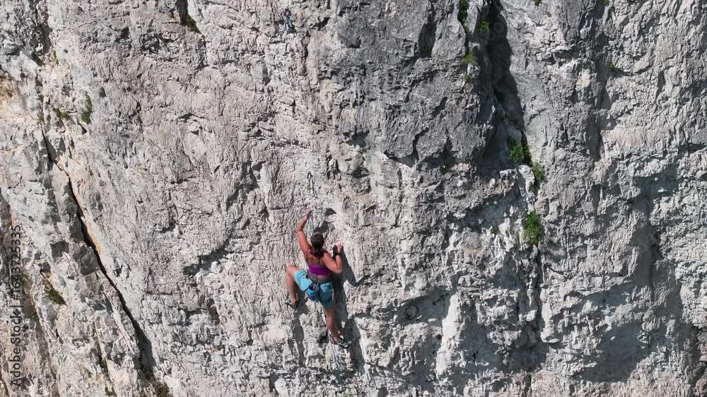 AERIAL: Brave woman in her climbing gear searches for good grip, as she navigates a difficult section of a rock wall. Her focus and body position illustrate the skill and physical demands of the climb AERIAL: Brave woman in her climbing gear searches for good grip, as she navigates a difficult section of a rock wall. Her focus and body position illustrate the skill and physical demands of the climb