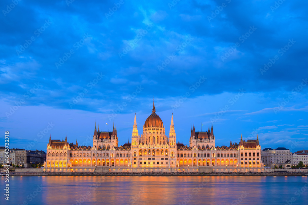 Fototapeta premium The majestic Parliament Building in Budapest illuminates the twilight sky, reflecting in the Danube River. This architectural wonder is a symbol of Hungary's rich history and culture.