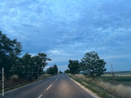 Landscape of a road in dim light at sunset, perspective, cloudy sky. 