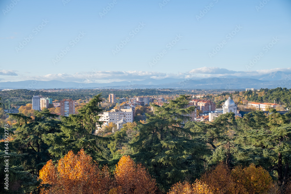 Fototapeta premium Colorful autumn landscape showcasing city skyline and distant mountains in a clear blue sky during daylight