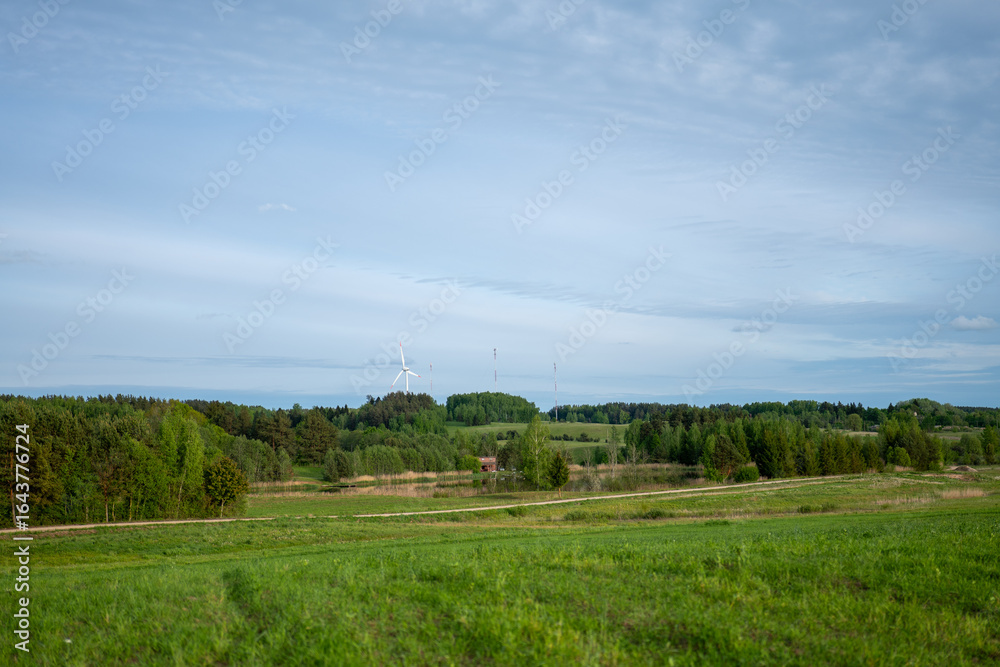 Obraz premium Wind turbine stands tall among green fields and forests in a rural landscape on a clear day