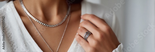 Close-up of a woman wearing silver necklaces and rings, showcasing modern jewelry design. Soft lighting enhances the elegance and style.