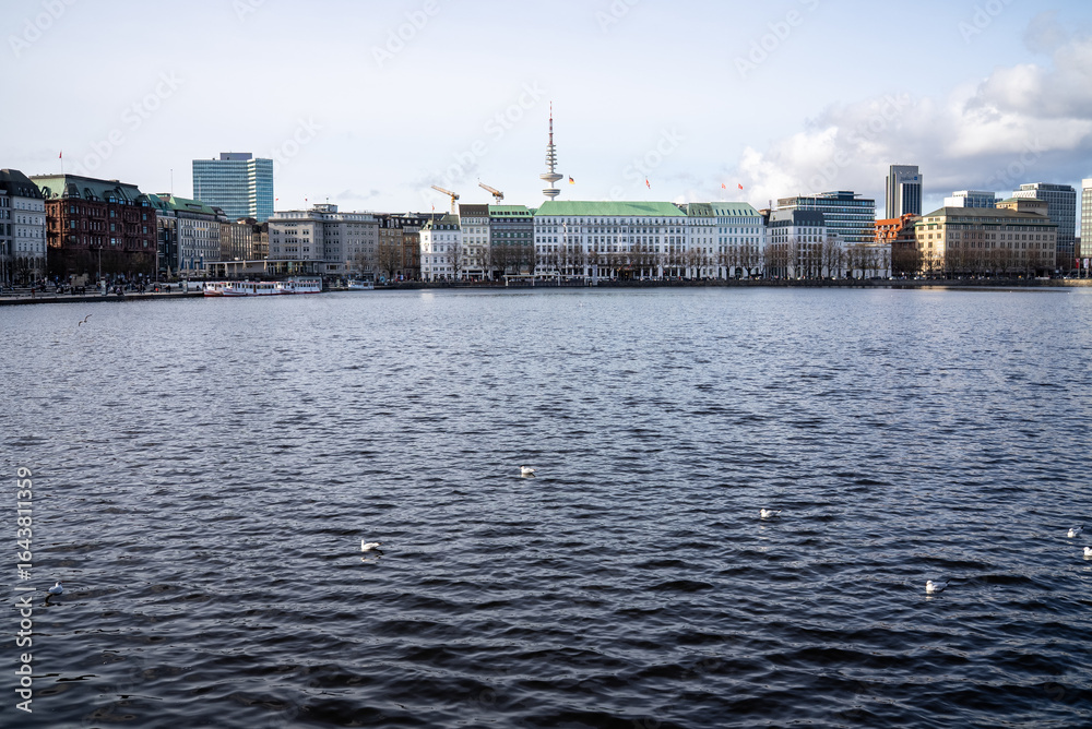 Obraz premium Cityscape by the waterfront showcases modern buildings and serene water surrounded by urban activity in Hamburg, Germany on a clear day