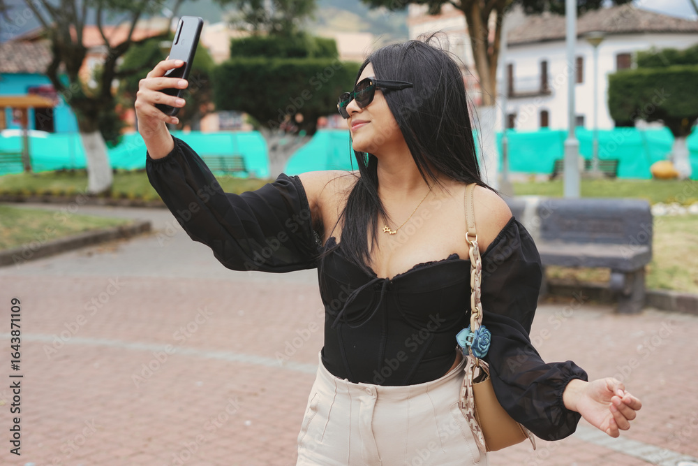 Naklejka premium Young latin woman taking a selfie in a town square