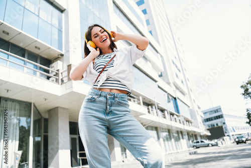 Tableau sur toile Young woman enjoying music outdoors in urban setting, smiling in casual outfit