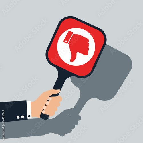 Human hand holding a red paddle with a thumbs down symbol casting a shadow showing disapproval or negative feedback