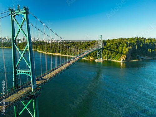 aerial view of Lions Gate Bridge in Vancouver, Canada during sunset with a blue sky, ocean, and mountains at distance