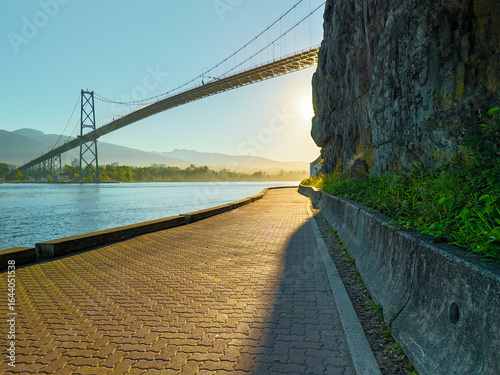 a photo with a bridge, the bay on the left and a cliff on the right during sunrise in Stanley Park in Vancouver