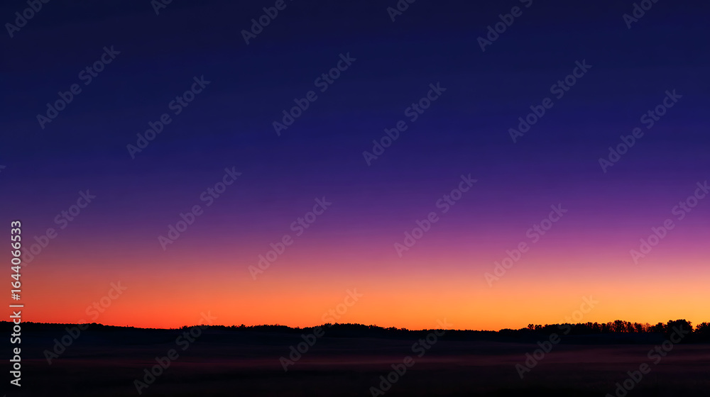 Fototapeta premium Deep indigo sky fades into vibrant orange horizon over silhouetted treeline sunset twilight