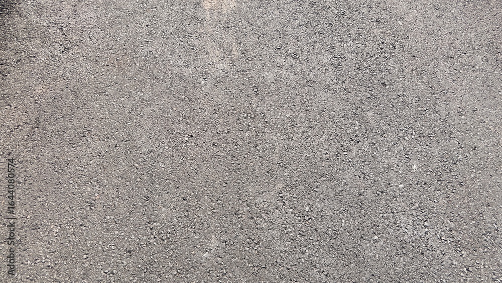 Fototapeta premium Close-up view of a textured asphalt surface with small stones and gravel.