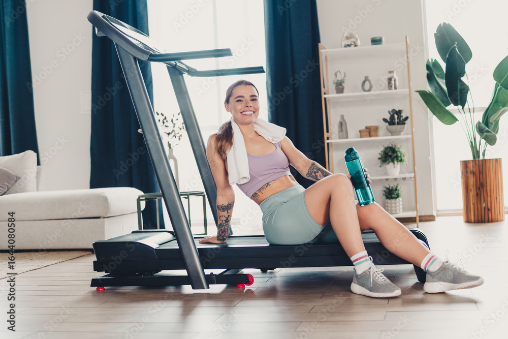 Fototapeta premium Sportsperson smiling after workout, sitting on a treadmill at home, showing active lifestyle and fitness dedication
