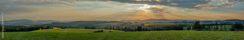 Fototapeta premium Sunset on summer hot grain field and green meadow in Krkonose mountains