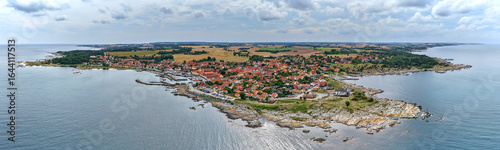 Aerial panoramic view of Svaneke on Bornholm Island Denmark surrounded by the Baltic Sea with red rooftops rocky coastline and lush countryside under a cloudy summer sky