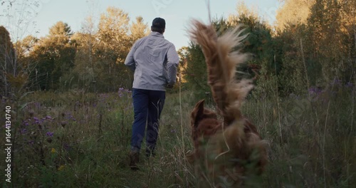 Man jogging through tall grass field with golden retriever dog in the Fall Vermont