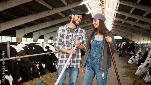 Valokuva Young happy Caucasian workers on animal farm standing in barn and talking and holding tools