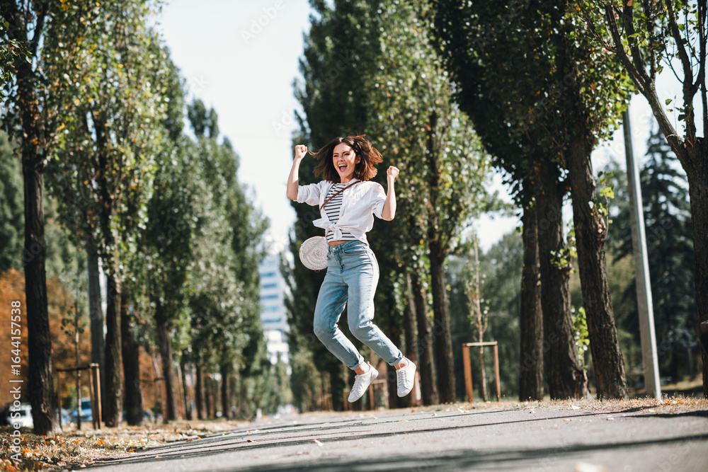 Obraz premium Joyful young woman jumping in the air on sunny day in the park