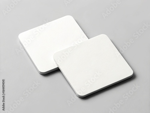Two blank white square coasters on a gray background