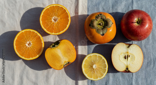 Top view of orange and lemon halves with persimmon, apple on white and blue background, panoramic