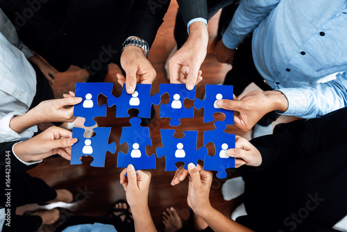 Quadro su tela Diverse professionals collaboratively holding blue puzzle pieces that symbolize networking, connection, and partnership in a corporate environment, demonstrating teamwork and unity