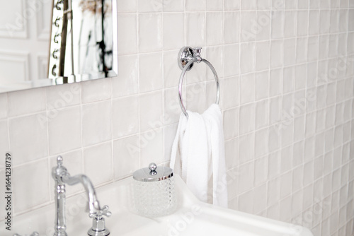white towel on round iron holder against white tiles and sink with mirror in bathroom