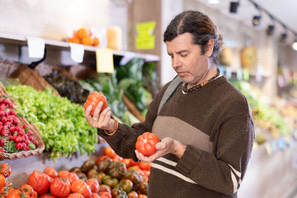 Adult man buyer choosing fresh tomatoes in vegetable shop Adult man buyer choosing fresh tomatoes in vegetable shop