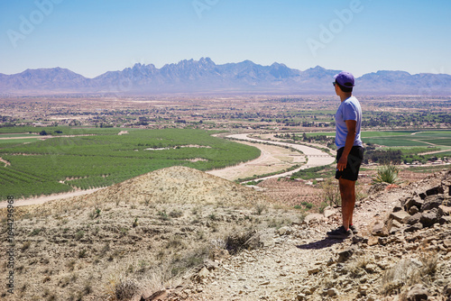 Lone hiker stands on a hiking trail in the Prehistoric Trackways National Monument on the Robledo Mountains overlooking agricultural fields and the Organ Mountains in Las Cruces, New Mexico 